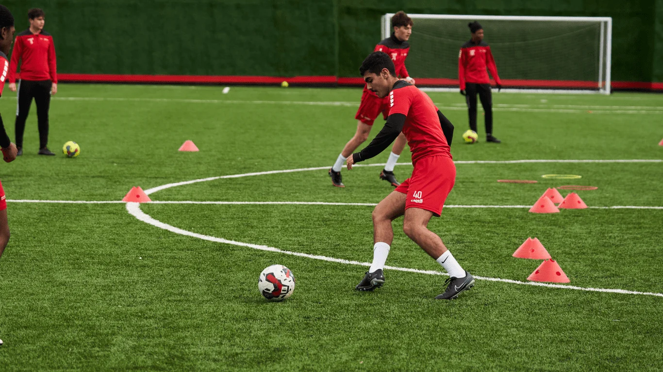 Jugadores aplicando un ejercicio con balón y conos en el campo